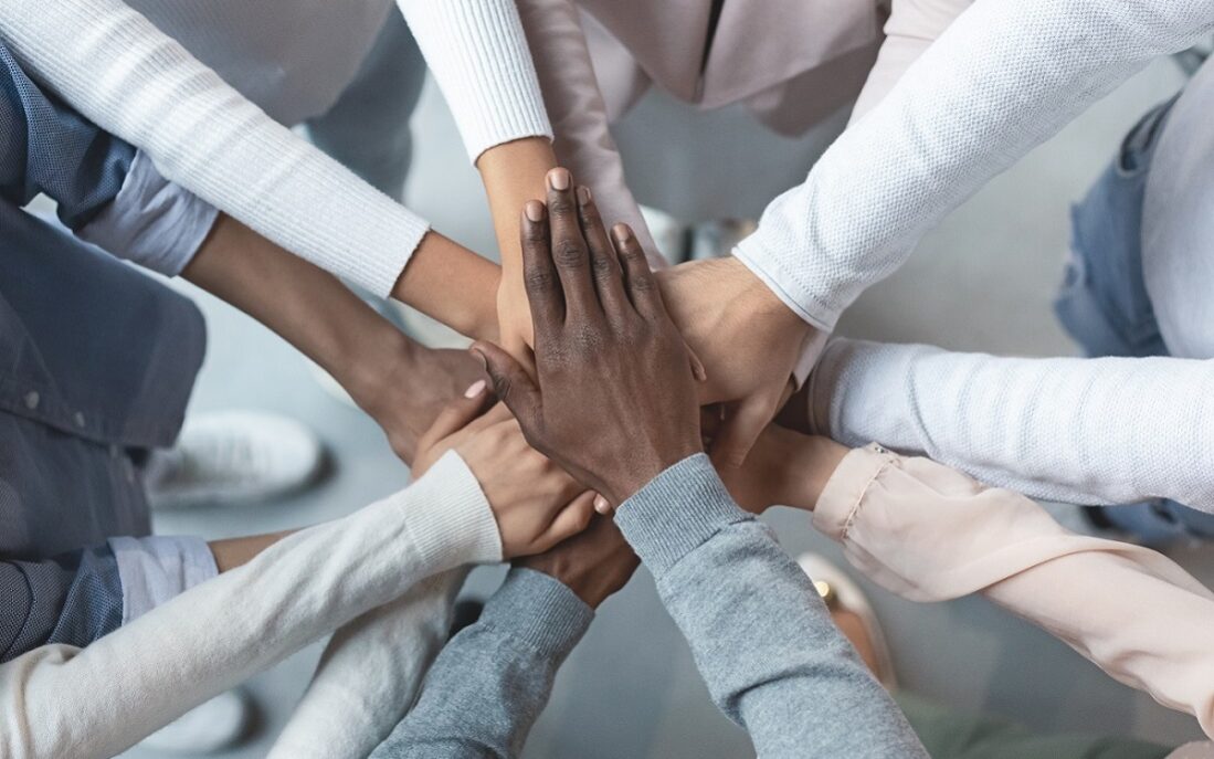 ©Prostock/Getty Photo of a group of diverse colleagues putting their hands together.