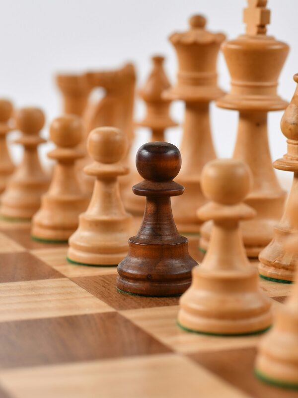 One dark brown chess piece stands out on a board of light brown chess pieces
