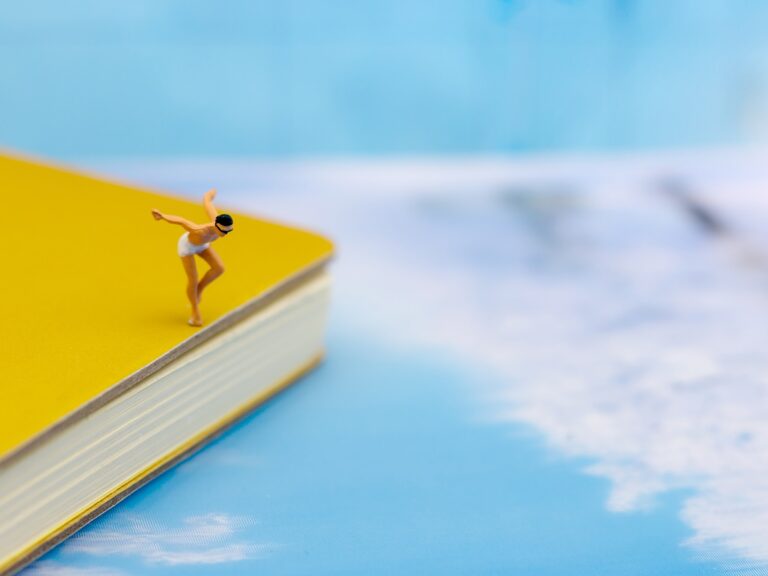 Photo of a male figurine wearing a bathing suit about to dive of a book in to a pretend ocean.