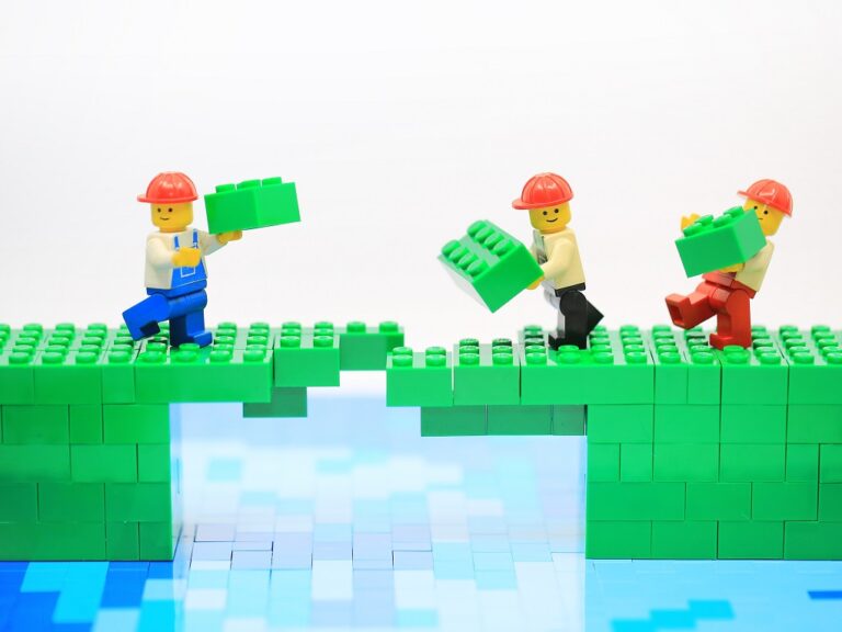 Lego figures are working together to build a bridge out of legos
