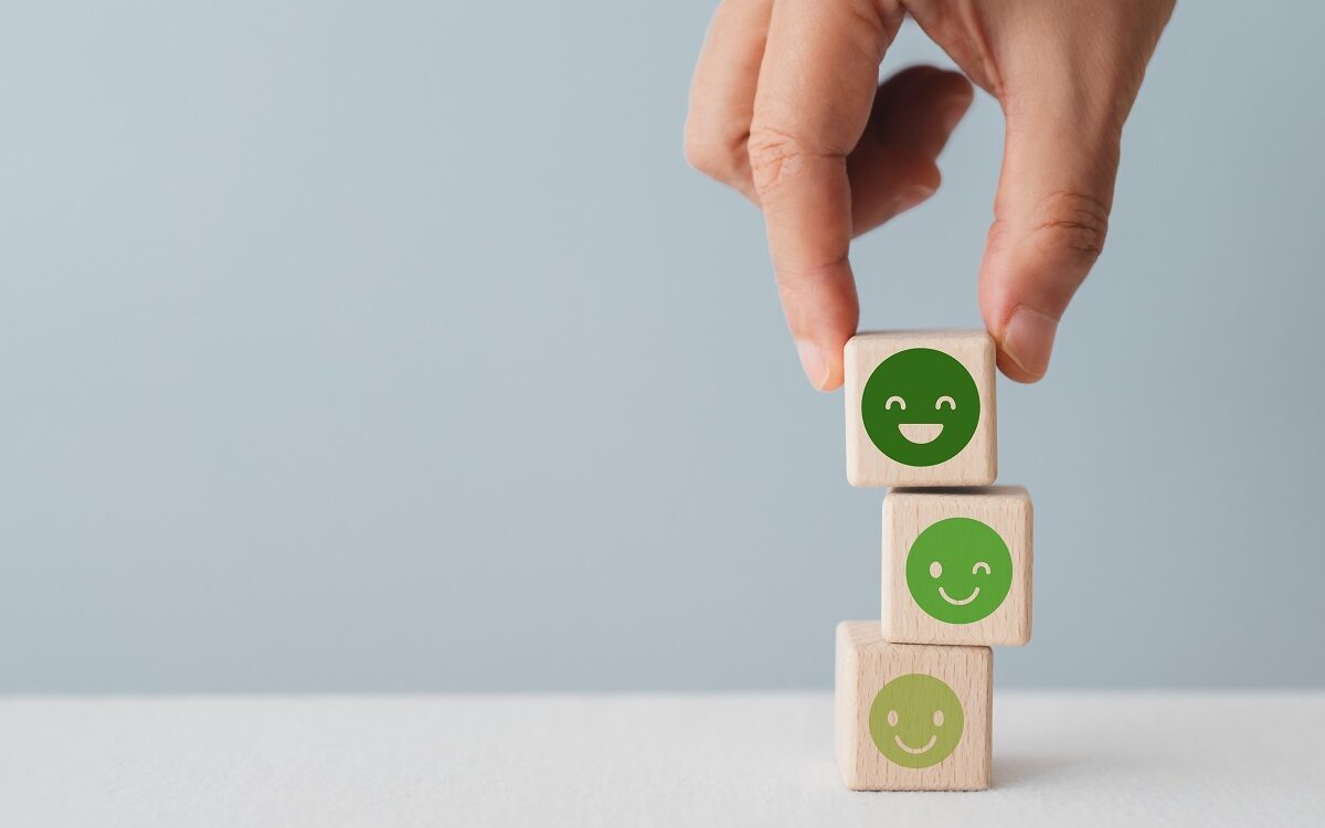 A stack of 3 wooden blocks with happy faces on them that get progressively deeper green and happier as they move up the stack