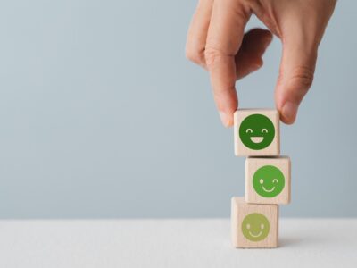 A stack of 3 wooden blocks with happy faces on them that get progressively deeper green and happier as they move up the stack