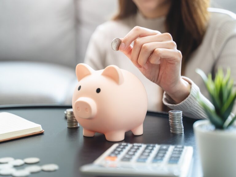 Young woman saving her monthly allowance puts the coin in the piggy bank on the table.