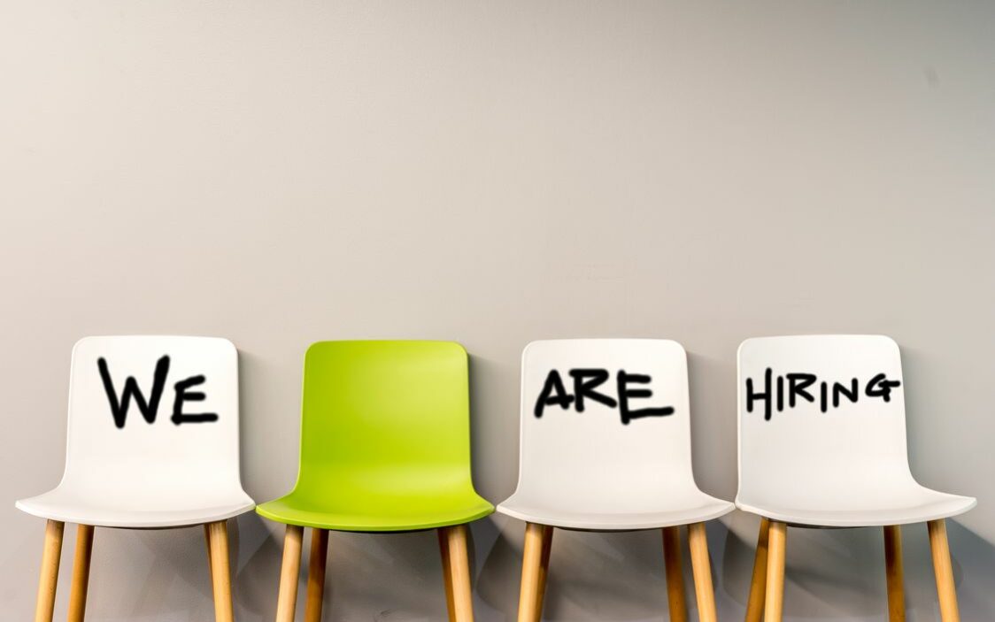 ©Nitsawan Katerattanakul / Shutterstock A row of 4 chairs with the writing "we are hiring" on the first, third, and fourth chairs which are white, but on the second chair, which is green it is left blank to signify that there is a seat availablein the company.