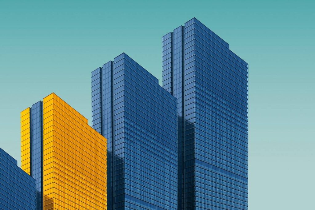 Four buildings in a row on a light blue background, three buildings are a normal grey color and one building is in yellow.
