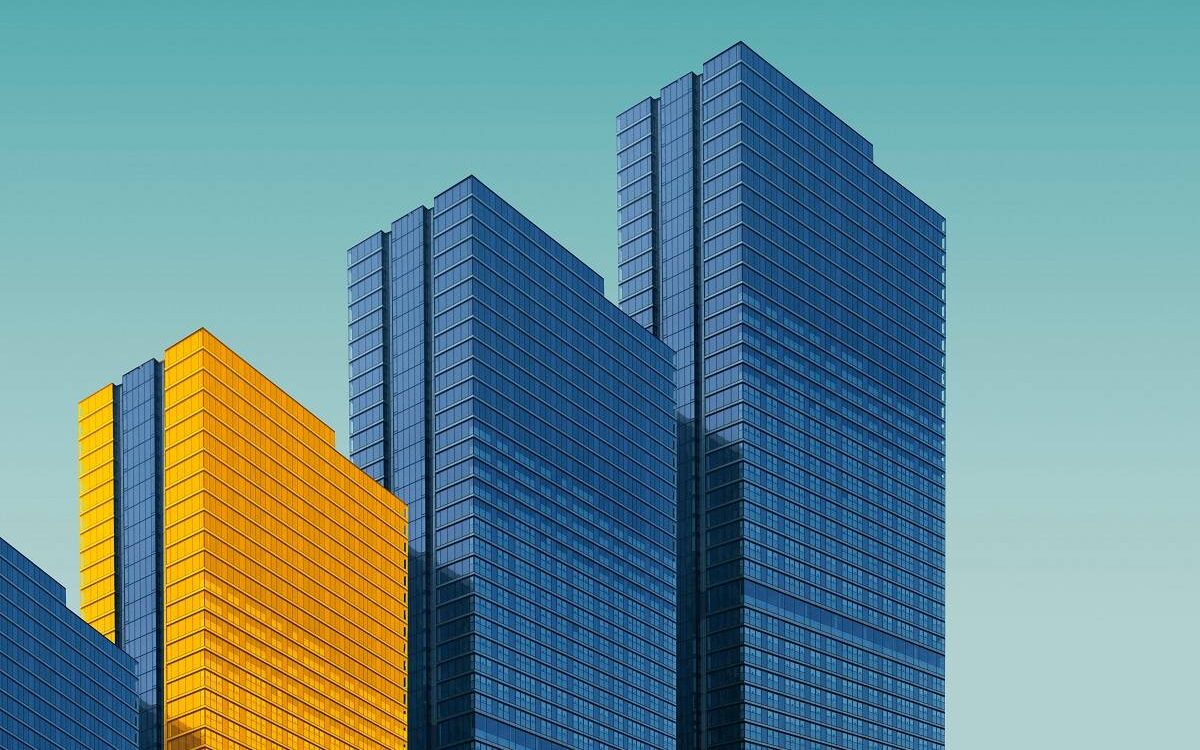 Four buildings in a row on a light blue background, three buildings are a normal grey color and one building is in yellow.