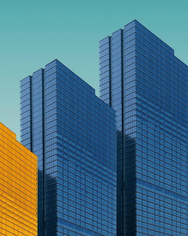 Four buildings in a row on a light blue background, three buildings are a normal grey color and one building is in yellow.