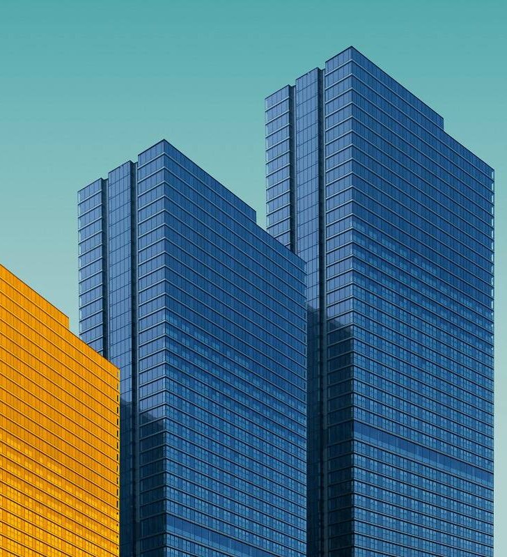 Four buildings in a row on a light blue background, three buildings are a normal grey color and one building is in yellow.