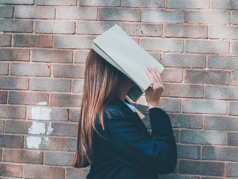 Woman covering her face with an open book, © Siora Photography / Unsplash