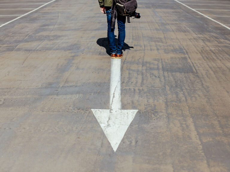 Person standing on arrow sign on road, ©Smart / Unsplash