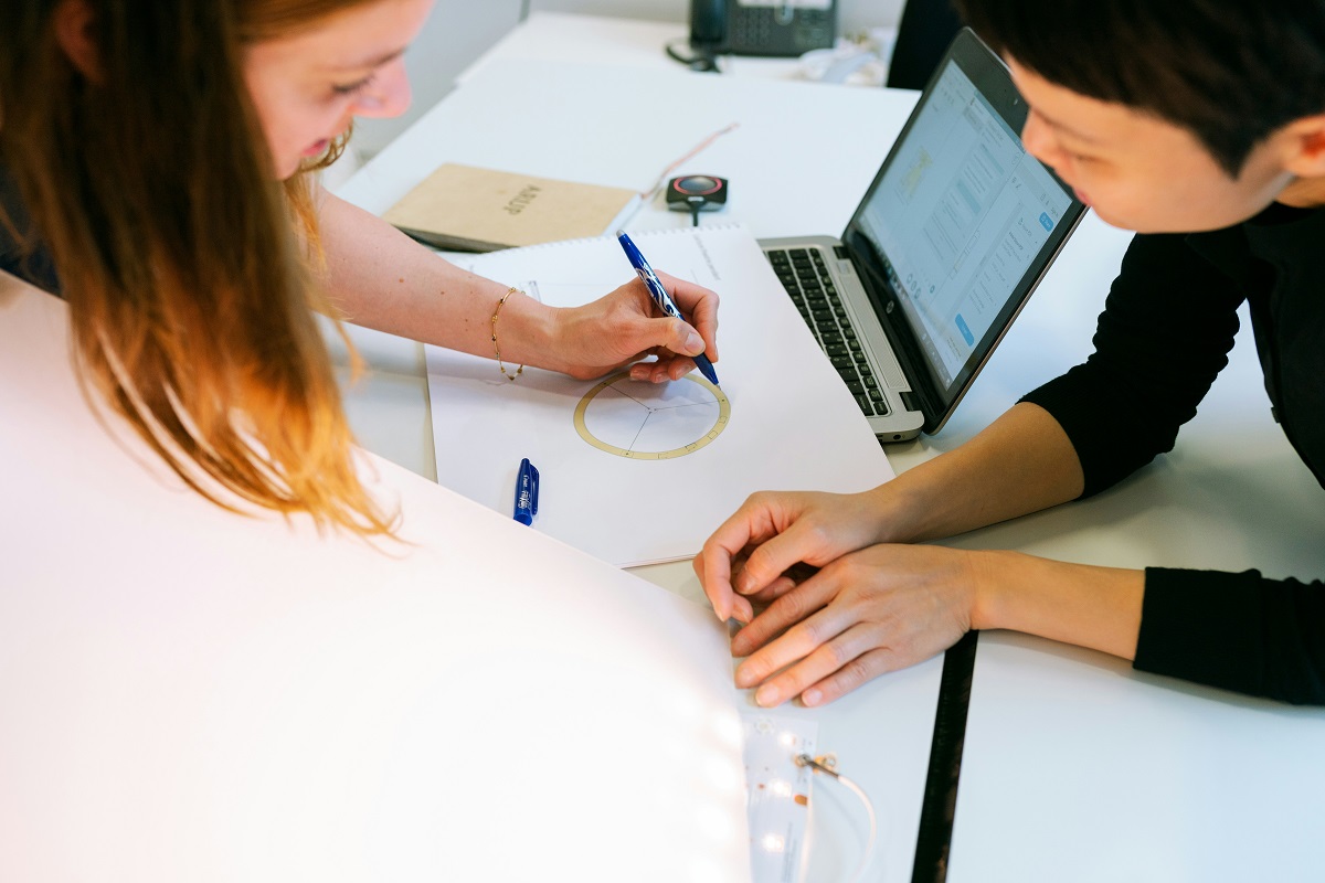Two people lean over a drawing working on an idea together
