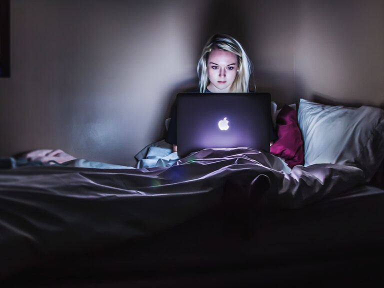 Woman teleworking on a bed in the dark.