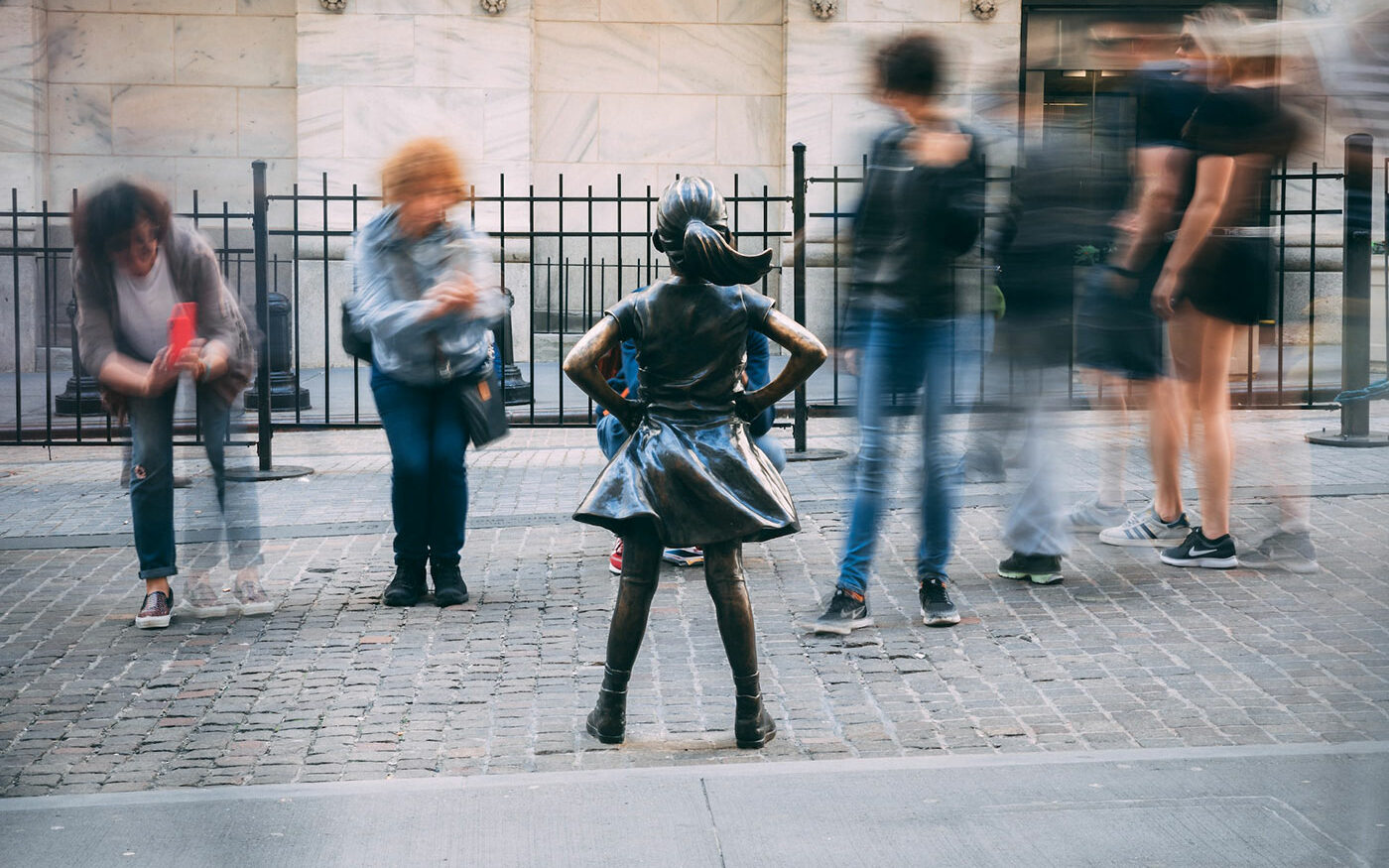 ©Christian Lendl/Unsplash Photo of the Fearless Girl statue in New York City. She is having her photo taken by tourists.
