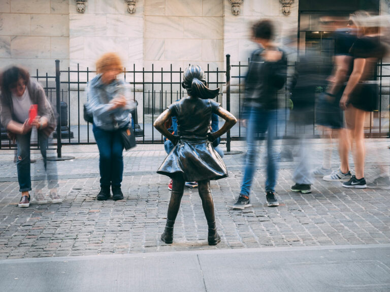 Photo of the Fearless Girl statue in New York City. She is having her photo taken by tourists.