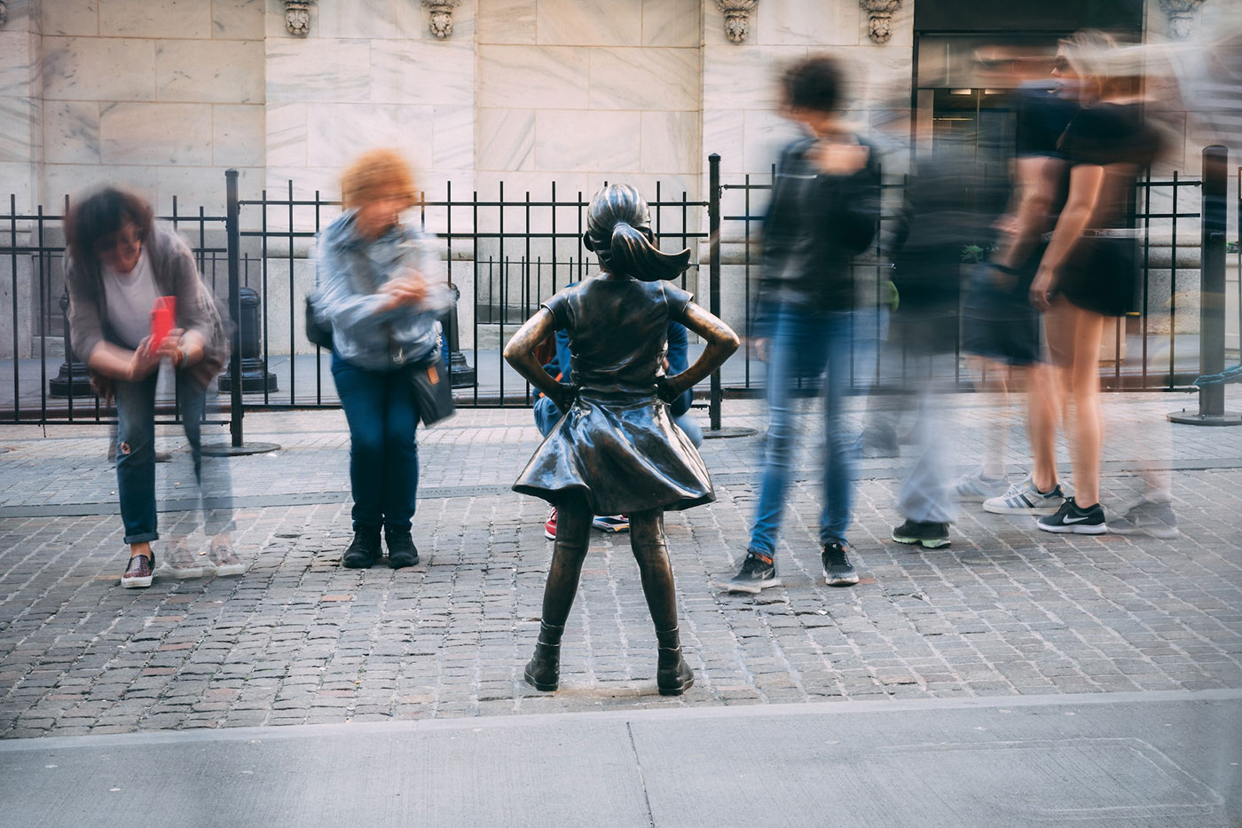 Photo of the Fearless Girl statue in New York City. She is having her photo taken by tourists.