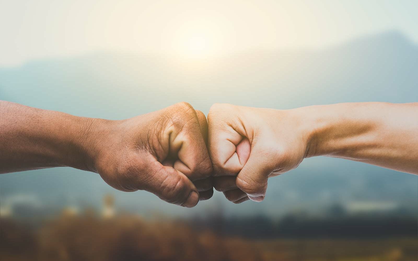 Feature photo by Worawut/AdobeStock Man giving fist bump in sun rising nature background.