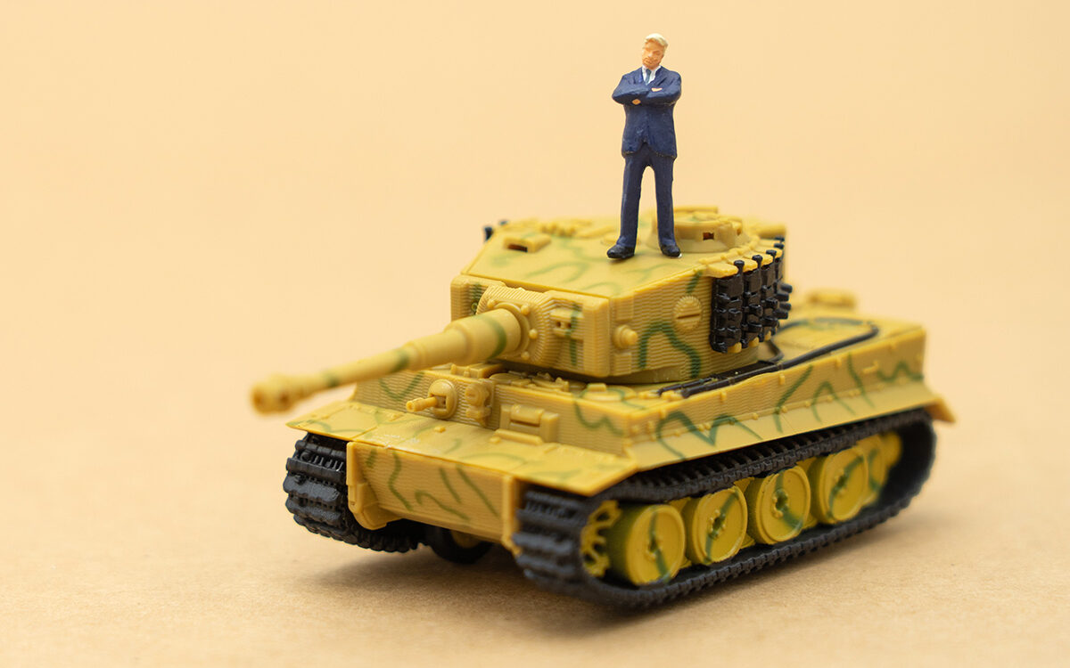 zasabe-AdobeStock Miniature people businessmen standing with a Tank model on the back Negotiating in business.