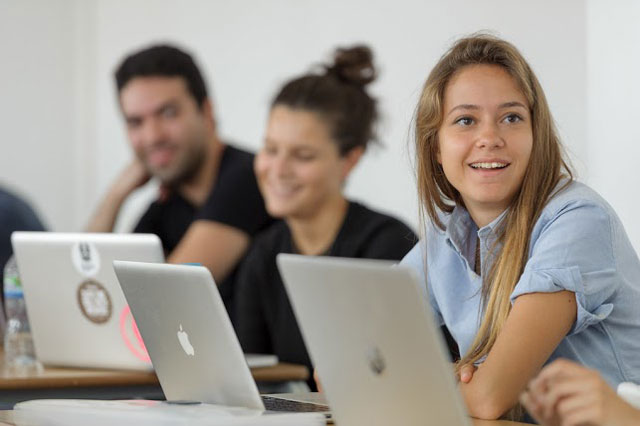 Three students in a classroom, each in front of a laptop